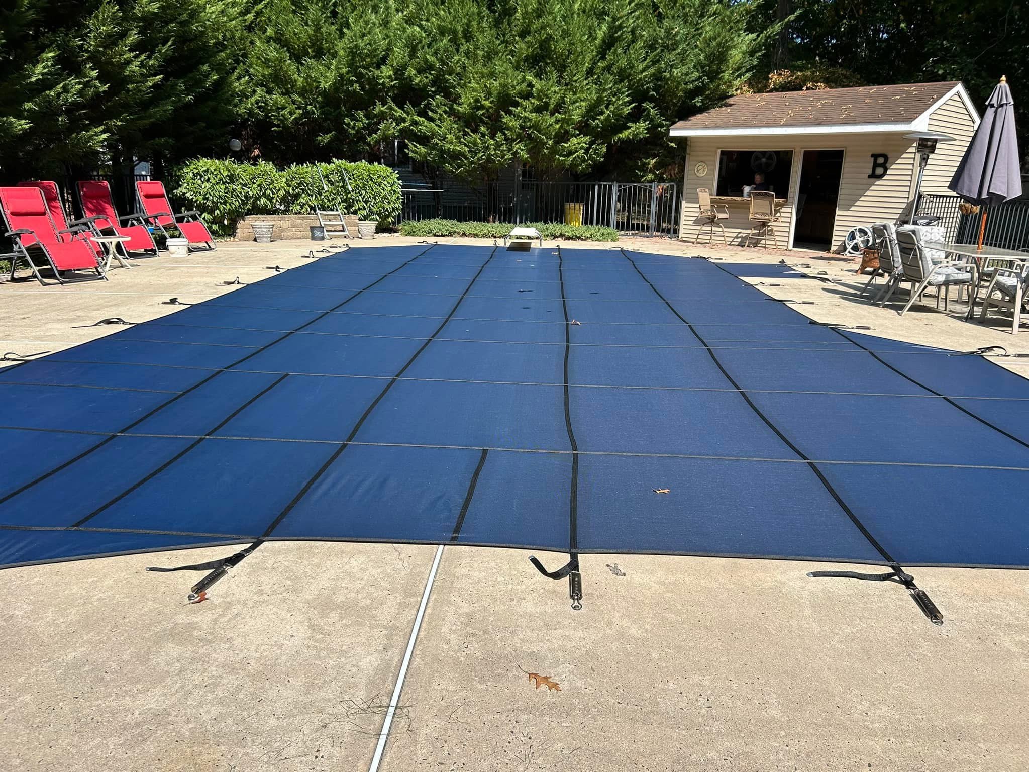 Blue safety cover installed with pool house in background